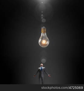 Searching for inspiration. Young businessman with hands spread looking at light bulb above his head