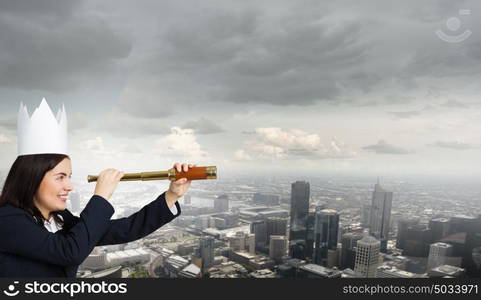 Searching perspective. Young businesswoman in paper crown looking in spyglass