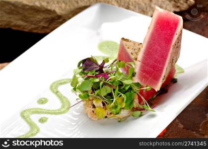 Seared ahi tuna fillets creatively stacked next to a side rice garnished with colorful sprouts. A green trail of wasabi sauce completes the plate.