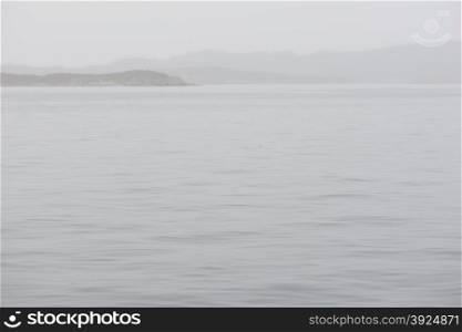 Seascape in Greenland on a foggy day with mountains, rain and calm water