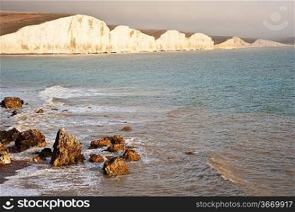 Seascape of receding waves with rocks in foreground and white cliffs in distance