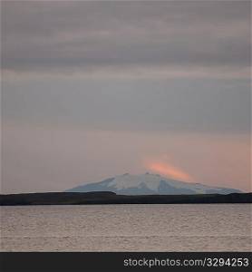 Seascape, snowy mountain in the rosy evening sunset
