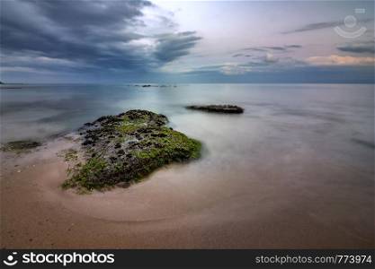 Seascape view of a calm sea with rocks with algae. Beauty sky with clouds at the horizon.