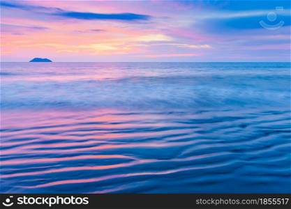 Seascape view of a tropical beach at sunset. Colourful sunset sky reflection on ocean waves and wavy sand beach textures. Tranquil beach at dusk. Long exposure. Blur motion.
