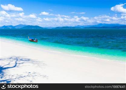 Seascape view of pure tropical island on sunny summer, abstract trees shadow on the white sand beach, fisherman steering fishing boat in the blue sea. Ranong, Thailand.