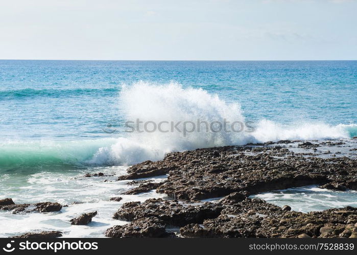 Seascape with rocky shore, surf waves and bright sky