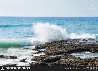 Seascape with rocky shore, surf waves and bright sky