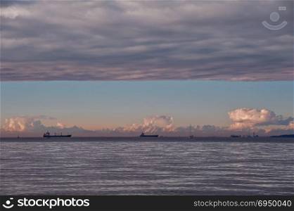 Seascape with ship at sunset with sky overcast and mountains in background.