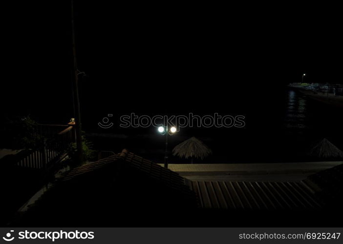 Seaside village on quiet summer night. Dark sea and pier with fishing boats illuminated by street lights.