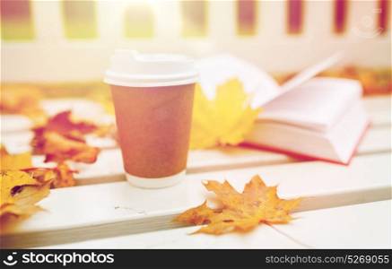 season, advertisement and drinks concept - coffee in paper cup on bench in autumn park. coffee drink in paper cup on bench at autumn park