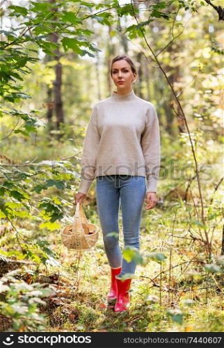 season and leisure people concept - young woman with mushrooms in wicker basket walking in forest. woman with basket picking mushrooms in forest