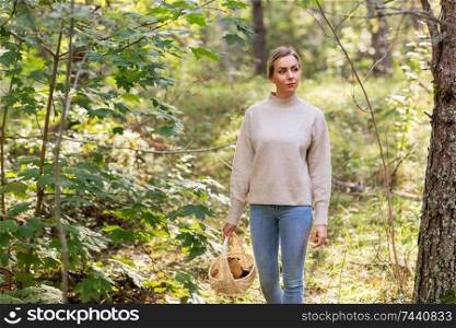 season and leisure people concept - young woman with mushrooms in wicker basket walking in forest. woman with basket picking mushrooms in forest