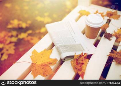 season and news concept - newspaper and coffee cup on bench in autumn park. newspaper and coffee cup on bench in autumn park