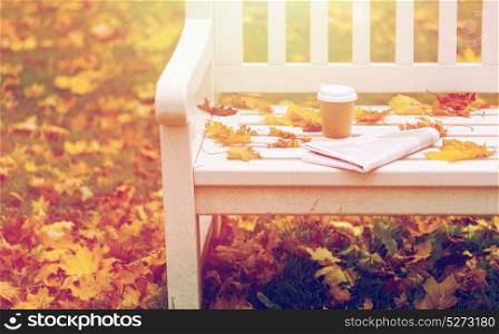 season and news concept - newspaper and coffee cup on bench in autumn park. newspaper and coffee cup on bench in autumn park