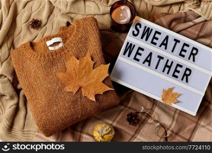 season and objects concept - wool clothes, autumn leaves, glasses and light box with sweater weather letters on warm blankets. light box with sweater weather letters in autumn