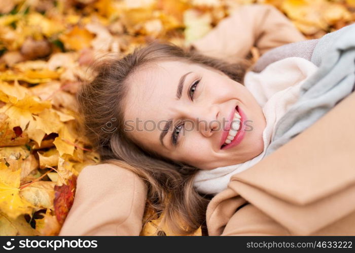 season and people concept - beautiful young woman lying on ground and autumn leaves. beautiful happy woman lying on autumn leaves