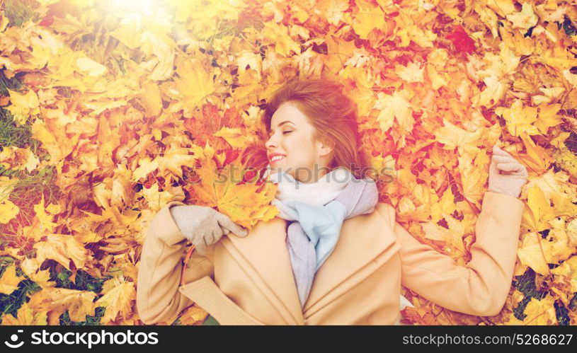 season and people concept - beautiful young woman lying on ground and autumn leaves. beautiful happy woman lying on autumn leaves