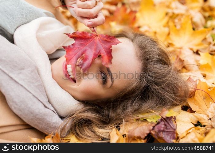 season and people concept - beautiful young woman with autumn maple leaf lying on ground. beautiful happy woman lying on autumn leaves