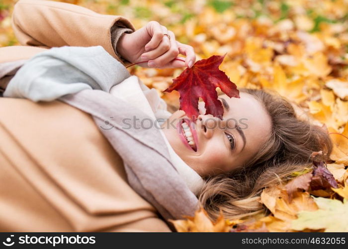 season and people concept - beautiful young woman with autumn maple leaf lying on ground. beautiful happy woman lying on autumn leaves