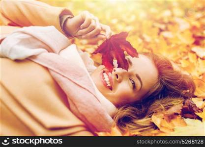 season and people concept - beautiful young woman with autumn maple leaf lying on ground. beautiful happy woman lying on autumn leaves