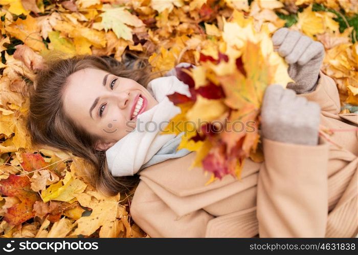 season and people concept - beautiful young woman with autumn maple leaves lying on ground. beautiful happy woman lying on autumn leaves