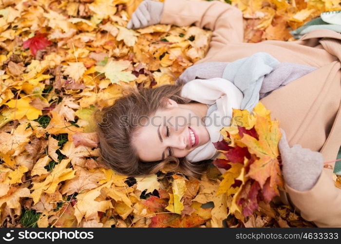 season and people concept - beautiful young woman with autumn maple leaves lying on ground. beautiful happy woman lying on autumn leaves