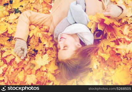 season and people concept - beautiful young woman with autumn maple leaves lying on ground. beautiful happy woman lying on autumn leaves