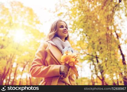 season and people concept - beautiful young woman with maple leaves walking in autumn park. beautiful woman with maple leaves in autumn park