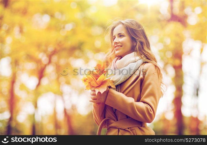 season and people concept - beautiful young woman with maple leaves walking in autumn park. beautiful woman with maple leaves in autumn park
