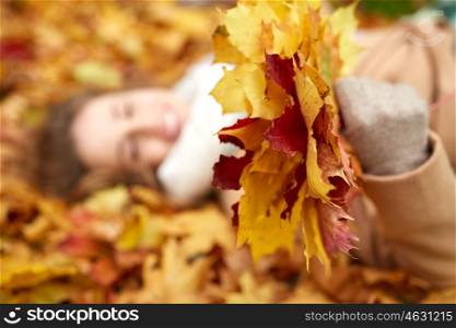 season and people concept - close up of beautiful young woman with autumn maple leaves lying on ground. close up of happy woman lying on autumn leaves