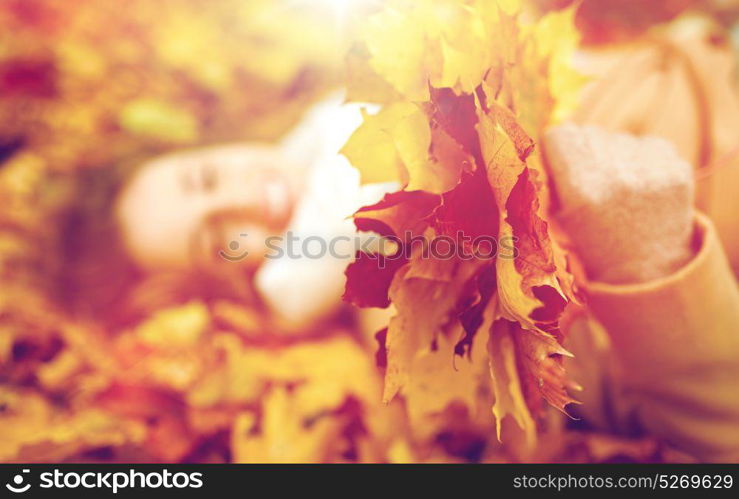 season and people concept - close up of beautiful young woman with autumn maple leaves lying on ground. close up of happy woman lying on autumn leaves