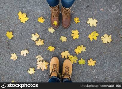 season and people concept - couple of feet in boots with autumn leaves on ground. couple of feet in boots and autumn leaves