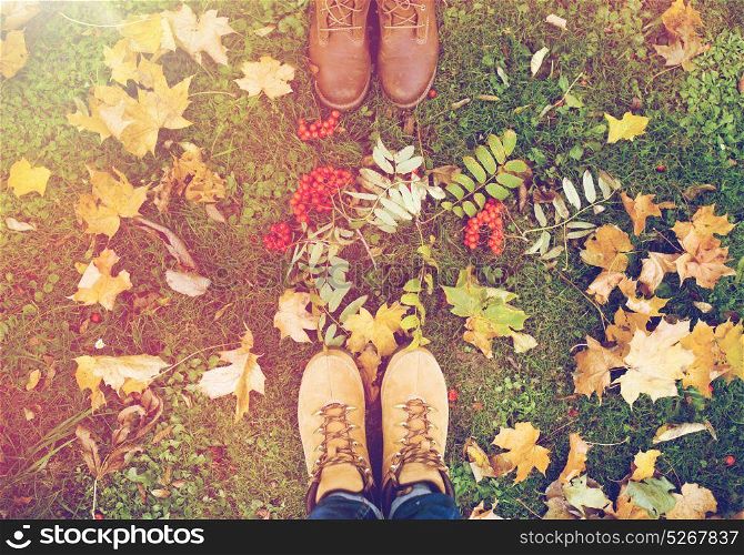 season and people concept - couple of feet in boots with rowanberries and autumn leaves on grass. feet in boots with rowanberries and autumn leaves