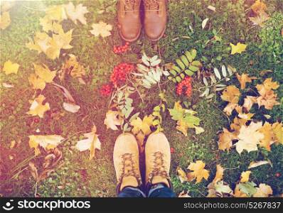 season and people concept - couple of feet in boots with rowanberries and autumn leaves on grass. feet in boots with rowanberries and autumn leaves