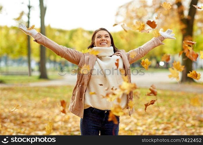season and people concept - happy young woman throwing maple leaves and having fun in autumn park. happy woman having fun with leaves in autumn park