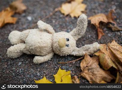 season, childhood and loneliness concept - lonely toy rabbit and autumn leaves on road or ground