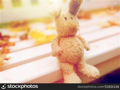 season, childhood and loneliness concept - lonely toy rabbit on bench in autumn park. toy rabbit on bench in autumn park