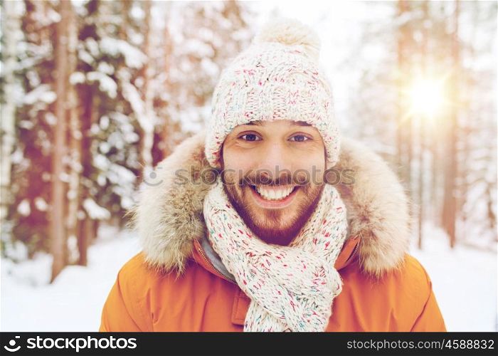 season, christmas and people concept - happy smiling young man in snowy winter forest