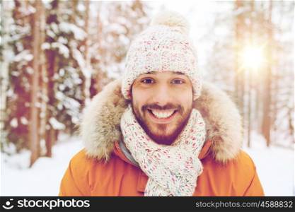 season, christmas and people concept - happy smiling young man in snowy winter forest