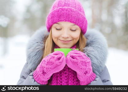 season, christmas, drinks and people concept - happy smiling young woman with cup drinking hot tea in winter forest