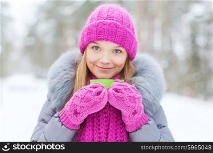 season, christmas, drinks and people concept - happy smiling young woman with cup drinking hot tea in winter forest