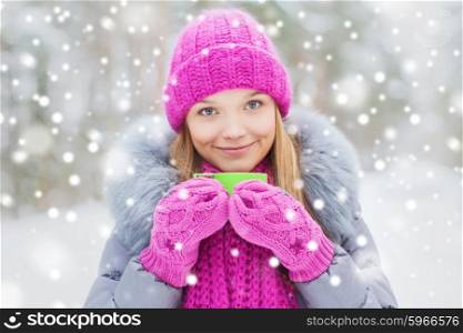 season, christmas, drinks and people concept - happy smiling young woman with cup drinking hot tea in winter forest. smiling young woman with cup in winter forest