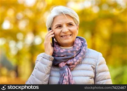 season, communication and people concept - happy senior woman calling on smartphone at autumn park. senior woman calling on smartphone at autumn park