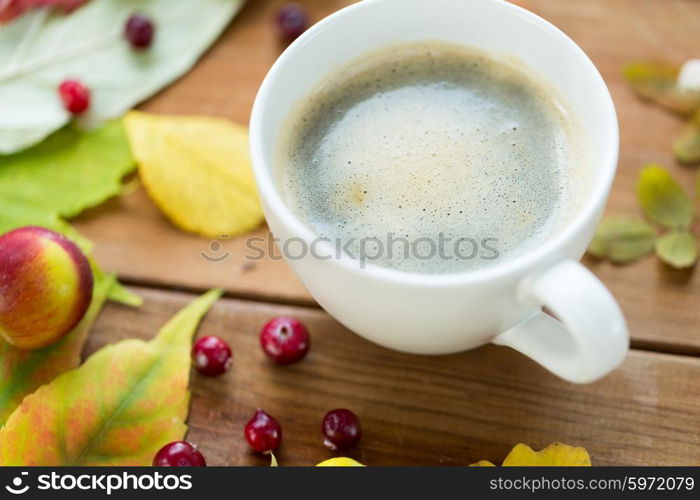 season, drink and morning concept - close up of coffee cup on wooden table with autumn leaves