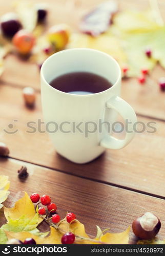 season, drink and morning concept - close up of tea cup on wooden table with autumn leaves