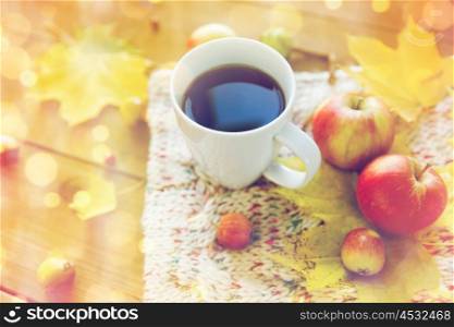 season, drink and morning concept - close up of tea cup on wooden table with autumn leaves and scarf