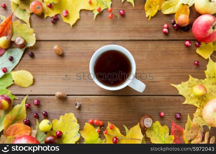 season, drink and morning concept - close up of tea cup on wooden table with autumn leaves
