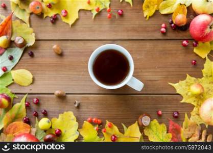 season, drink and morning concept - close up of tea cup on wooden table with autumn leaves