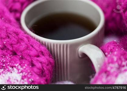 season, drinks, christmas and winter holidays concept - close up of tea or coffee mug and knitted woolen scarf in snow