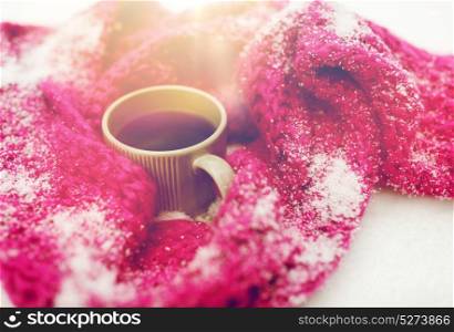 season, drinks, christmas and winter holidays concept - close up of tea or coffee mug and knitted woolen scarf in snow. close up of tea or coffee and winter scarf in snow